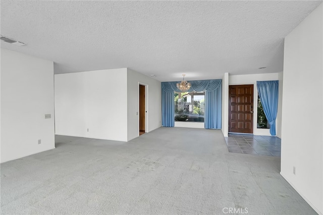 spare room featuring a textured ceiling, carpet floors, and an inviting chandelier