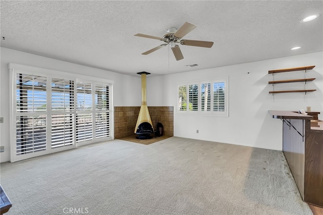 unfurnished living room with a wood stove, a textured ceiling, carpet, and ceiling fan