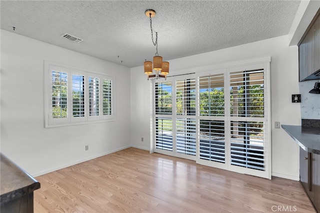 unfurnished dining area featuring light hardwood / wood-style flooring, a textured ceiling, and a chandelier