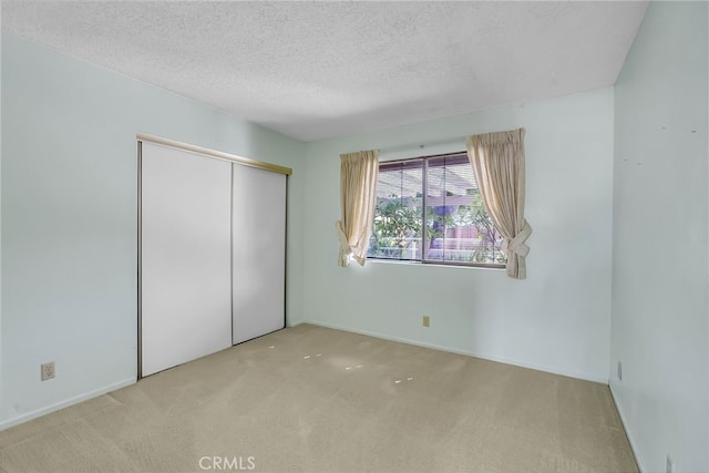 unfurnished bedroom featuring light carpet, a closet, and a textured ceiling