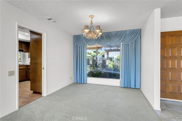 carpeted spare room with a textured ceiling and an inviting chandelier