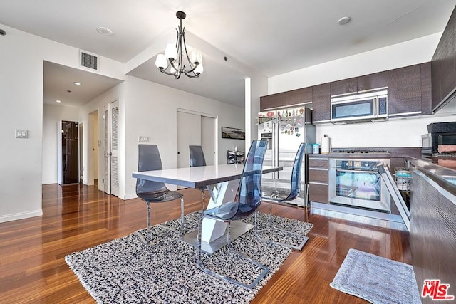 kitchen with dark wood-type flooring, an inviting chandelier, a breakfast bar area, dark brown cabinets, and stainless steel appliances