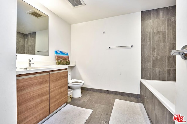 bathroom with vanity, hardwood / wood-style flooring, toilet, and tiled tub