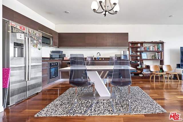 kitchen with dark wood-type flooring, sink, appliances with stainless steel finishes, a notable chandelier, and dark brown cabinetry