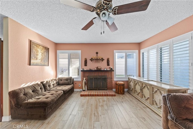 living room with ceiling fan, light wood-type flooring, a brick fireplace, and a textured ceiling