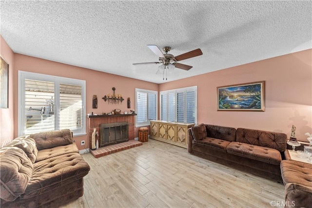 living room featuring ceiling fan, a fireplace, a textured ceiling, and light hardwood / wood-style floors