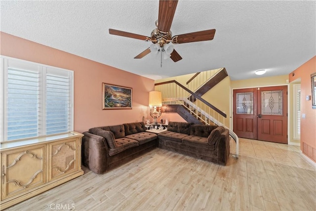 living room featuring ceiling fan, a textured ceiling, and light wood-type flooring