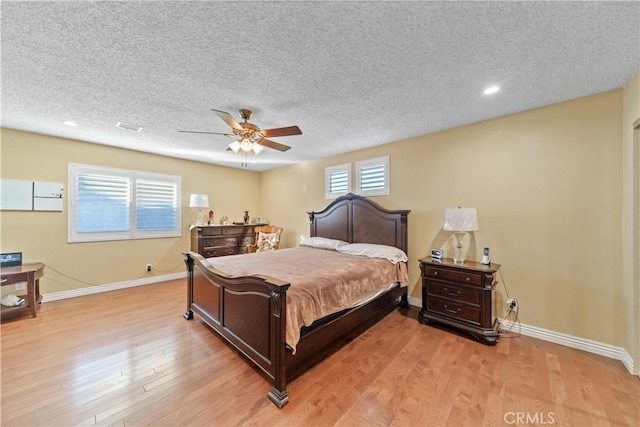 bedroom featuring ceiling fan, light hardwood / wood-style floors, multiple windows, and a textured ceiling