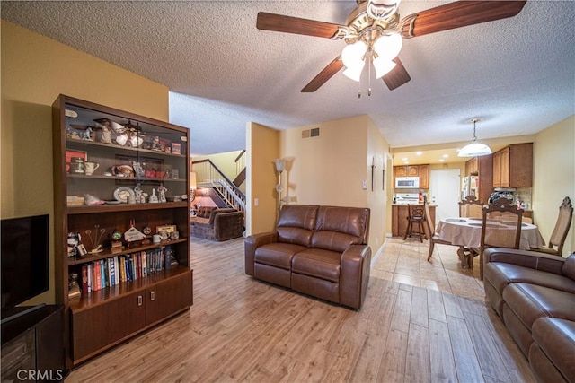 living room featuring ceiling fan, a textured ceiling, and light wood-type flooring