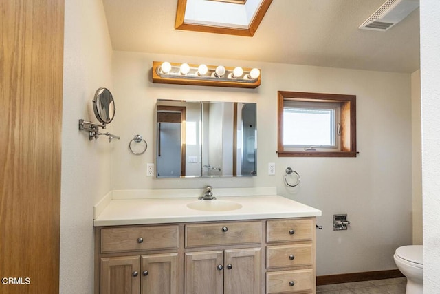 bathroom featuring tile patterned floors, vanity, a skylight, and toilet