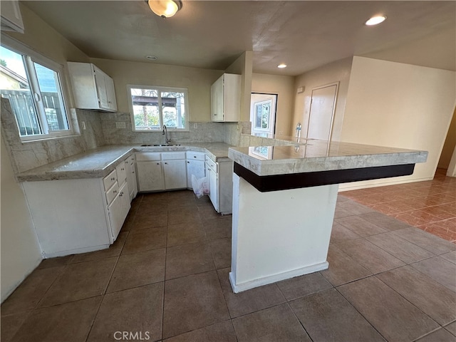 kitchen with kitchen peninsula, tasteful backsplash, a kitchen breakfast bar, white cabinetry, and sink