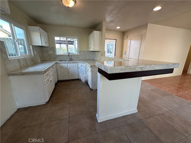 kitchen with kitchen peninsula, white cabinets, backsplash, a kitchen breakfast bar, and sink