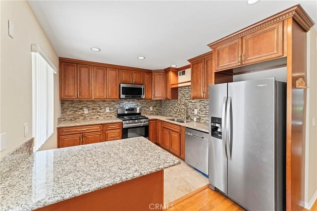 kitchen with light stone countertops, sink, stainless steel appliances, decorative backsplash, and light wood-type flooring