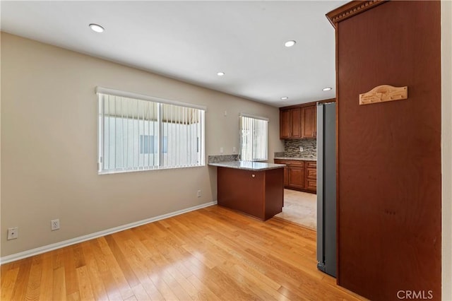 kitchen featuring stainless steel refrigerator, kitchen peninsula, backsplash, and light wood-type flooring