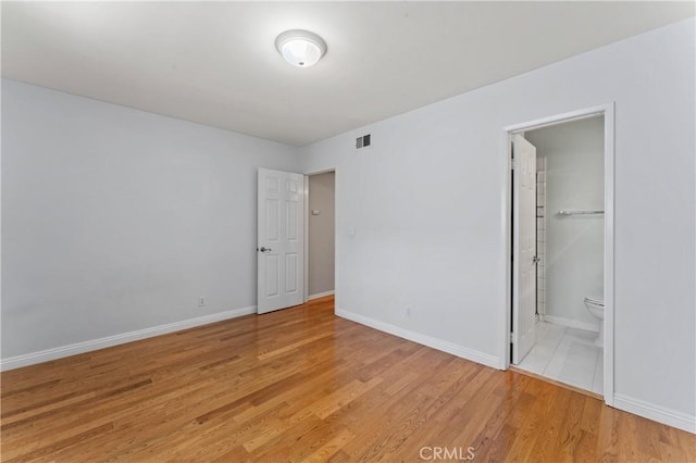 unfurnished bedroom featuring light hardwood / wood-style floors, a spacious closet, a closet, and ensuite bathroom