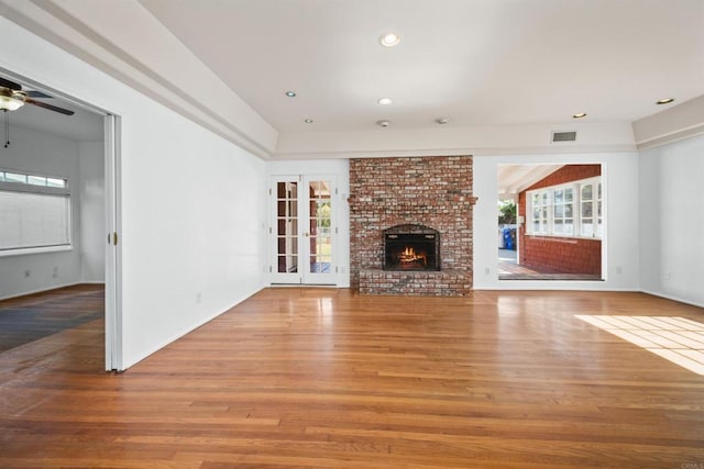 unfurnished living room with a brick fireplace, wood-type flooring, and ceiling fan