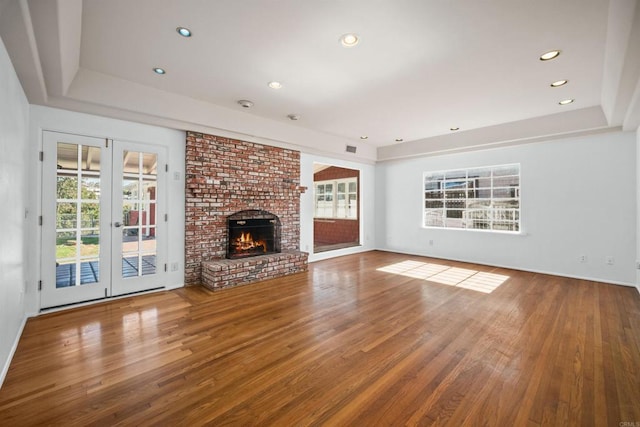 unfurnished living room with french doors, a tray ceiling, a fireplace, and hardwood / wood-style floors