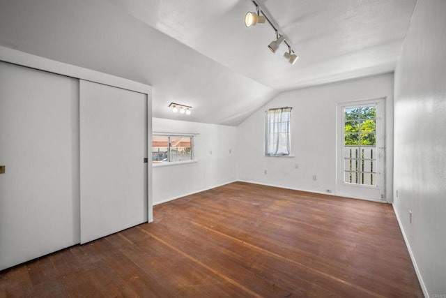 unfurnished bedroom with rail lighting, vaulted ceiling, and dark hardwood / wood-style flooring