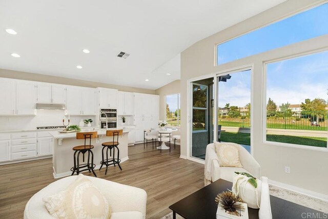 kitchen with white cabinetry, an island with sink, vaulted ceiling, and light wood-type flooring