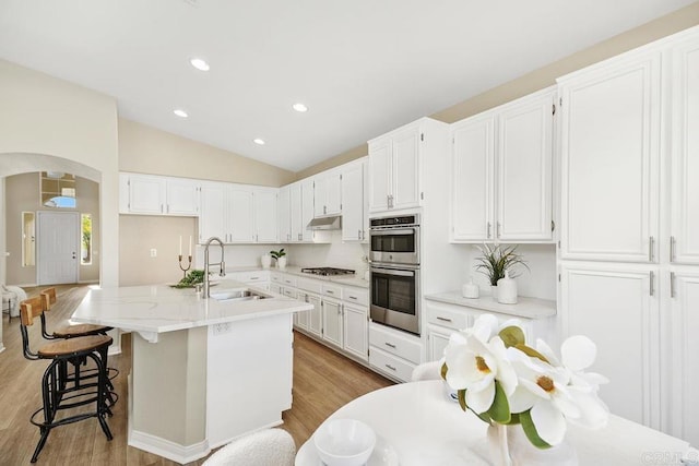 kitchen featuring light wood-type flooring, vaulted ceiling, sink, a center island with sink, and white cabinets