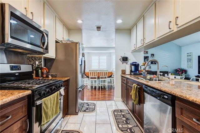 kitchen featuring dark brown cabinetry, light stone counters, sink, and stainless steel appliances