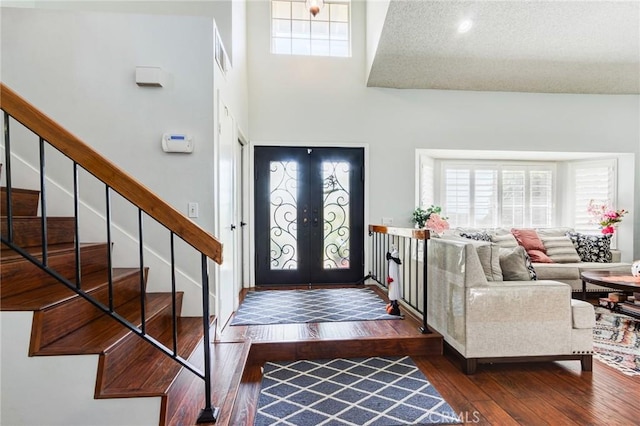 foyer entrance with a towering ceiling, french doors, a textured ceiling, and dark wood-type flooring