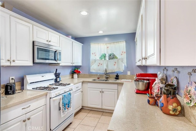 kitchen with light tile patterned flooring, white cabinetry, white gas range oven, and sink