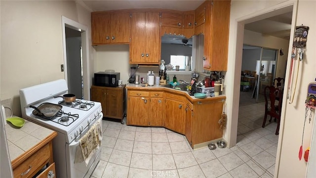 25626 Anderson Ave, Barstow, CA 92311 - kitchen featuring black microwave, brown cabinetry, white gas range, tile countertops, and light tile patterned floors