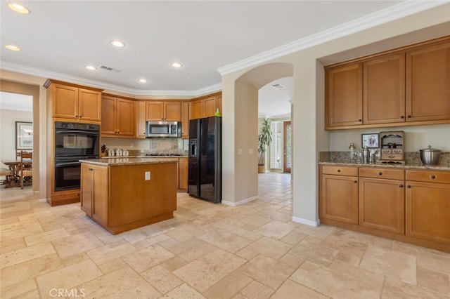 kitchen with light stone countertops, a kitchen island, ornamental molding, and black appliances