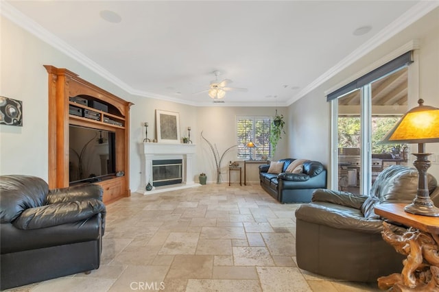 living area with stone tile floors, ornamental molding, a glass covered fireplace, ceiling fan, and baseboards