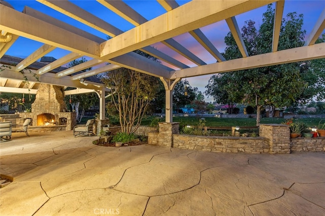 patio terrace at dusk with an outdoor stone fireplace and a pergola