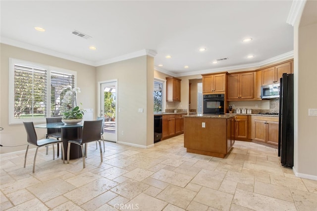 kitchen with visible vents, baseboards, a center island, black appliances, and stone tile flooring