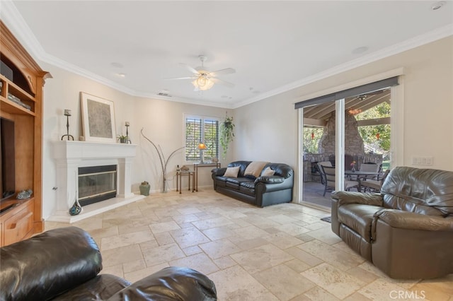 living room featuring stone tile floors, ornamental molding, ceiling fan, and a glass covered fireplace