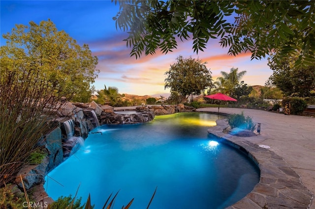 pool at dusk featuring pool water feature and a jacuzzi