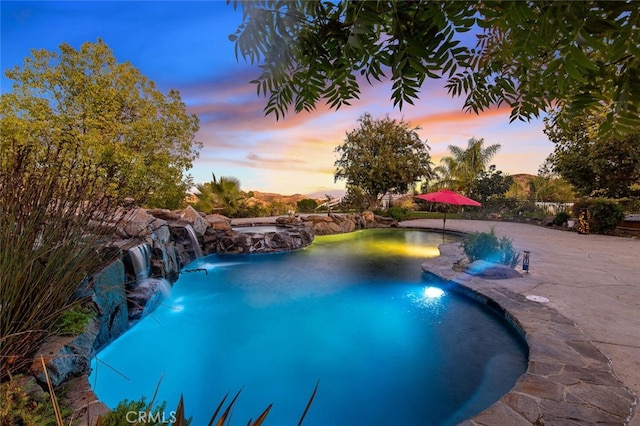 pool at dusk with a pool with connected hot tub