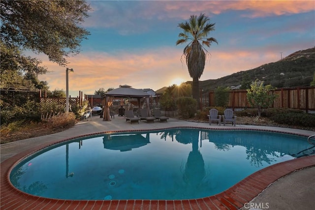 pool at dusk featuring a gazebo and a mountain view