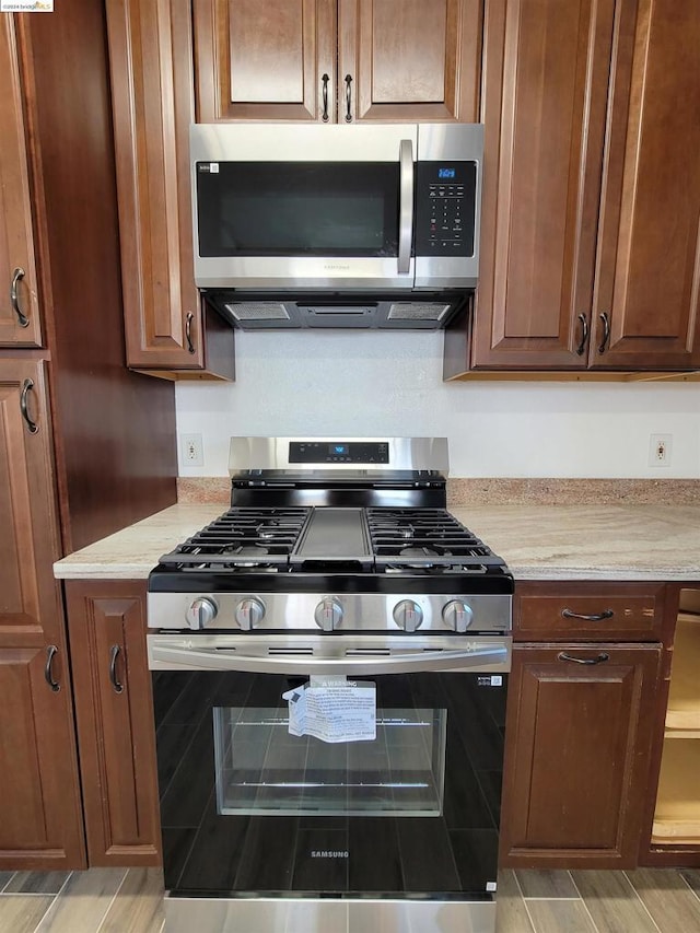 kitchen featuring appliances with stainless steel finishes, light hardwood / wood-style floors, and light stone counters