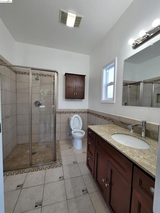 bathroom featuring tile patterned floors, toilet, a shower with door, vanity, and tile walls