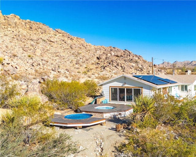 rear view of property featuring solar panels, a sunroom, a swimming pool with hot tub, a patio area, and a mountain view