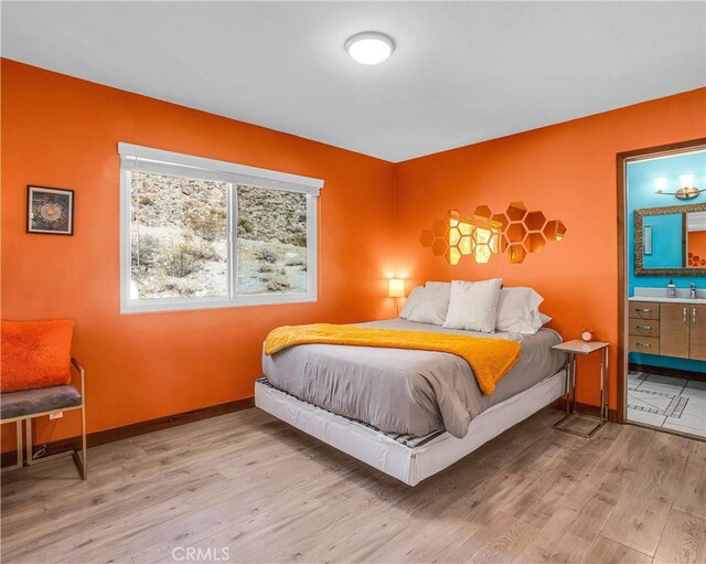 bedroom with baseboards, a sink, wood finished floors, and ensuite bathroom