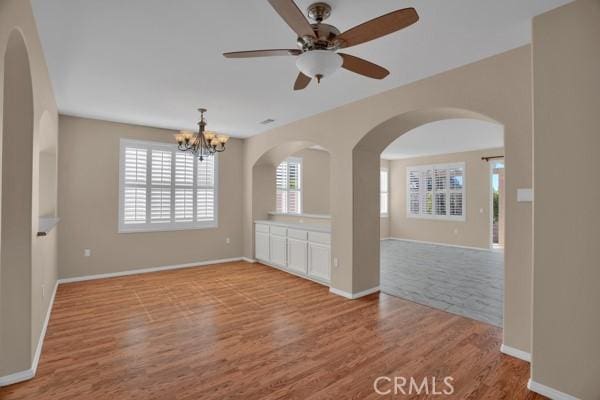 empty room featuring ceiling fan with notable chandelier and light hardwood / wood-style flooring