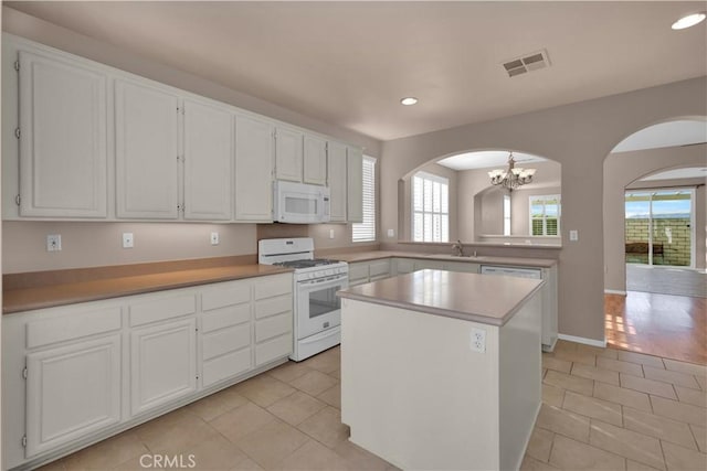 kitchen featuring white appliances, light hardwood / wood-style flooring, a notable chandelier, a center island, and white cabinetry