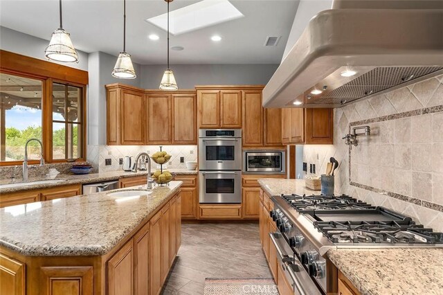 kitchen with custom exhaust hood, an island with sink, appliances with stainless steel finishes, light hardwood / wood-style flooring, and sink