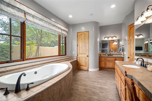 bathroom with vanity, a relaxing tiled tub, and a healthy amount of sunlight