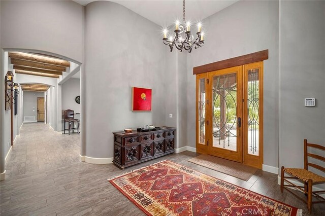 foyer featuring beam ceiling, a notable chandelier, hardwood / wood-style flooring, and a towering ceiling