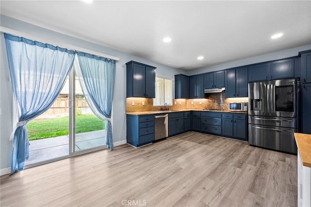 kitchen with backsplash, appliances with stainless steel finishes, a sink, blue cabinets, and under cabinet range hood