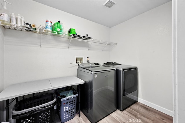 clothes washing area featuring washer and clothes dryer, visible vents, wood finished floors, laundry area, and baseboards