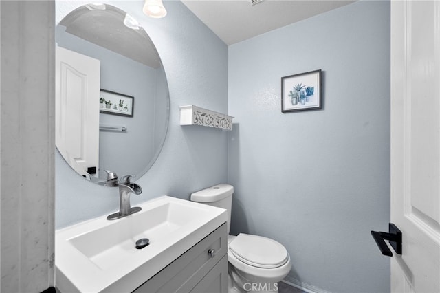 half bathroom featuring toilet, a textured wall, and vanity