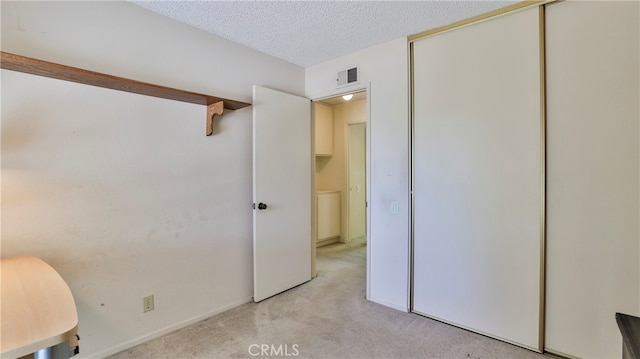 unfurnished bedroom with light carpet, a textured ceiling, and a closet