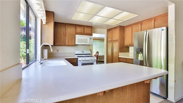 kitchen featuring a healthy amount of sunlight, sink, kitchen peninsula, and white appliances